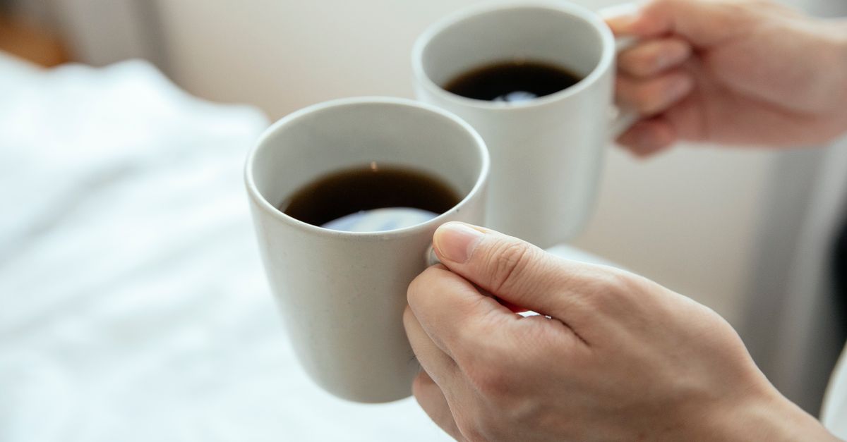 Close-up of hands holding two mugs filled with hot black coffee, perfect for a cozy morning.