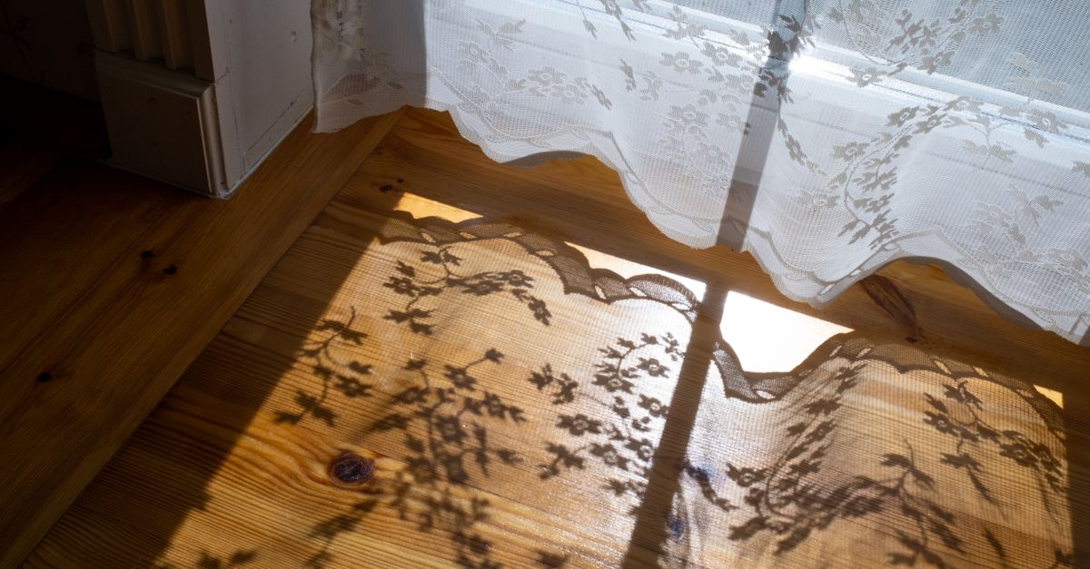 Lace curtains casting delicate floral shadows on a hardwood floor in warm sunlight, creating a vintage ambiance.