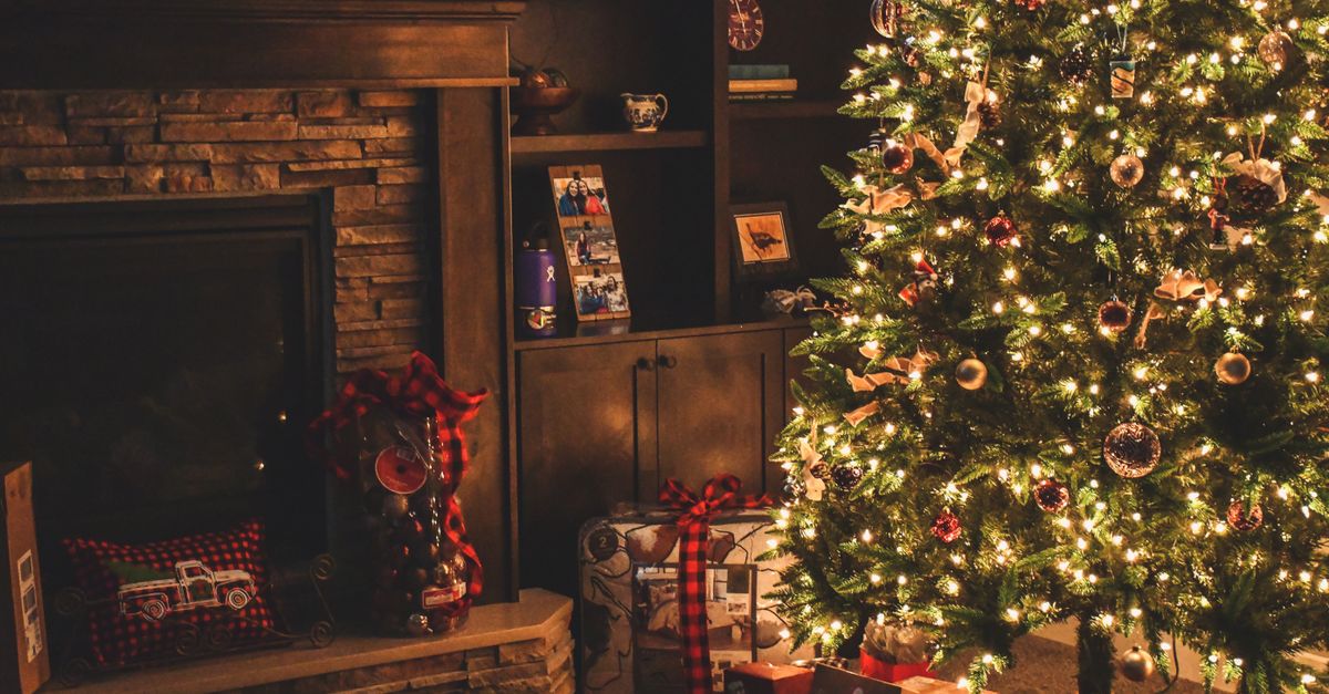 Warm holiday scene of a decorated Christmas tree with gifts by a cozy fireplace.