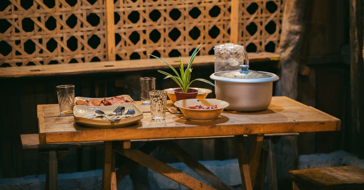 A rustic dining table set with plates, bowls, and a potted plant, creating a cozy indoor atmosphere.