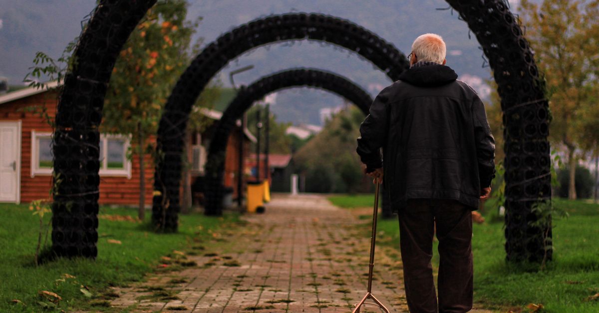 Senior man with cane walking through a scenic outdoor path under archways.